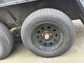 A black wheel with multiple holes and a rusty hubcap mounted on a trailer tire featuring a steel belted radial design
