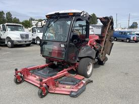 A red 2012 Toro Groundsmaster 5910 turf maintenance vehicle with a transparent cab and a front-mounted cutting deck is parked with its grass cutting blades visible