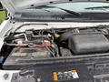The image shows the engine compartment of a 2024 Ford E-450 with visible components like the battery cables and engine parts