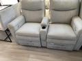A light-colored reclining sofa with two seats and a central armrest featuring a cup holder