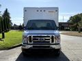 A 2021 Ford Econoline with a large box cargo area in the back and a chrome grille is positioned head-on with two front seats visible inside the cabin