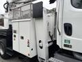A 2013 Freightliner 114SD truck with a white utility body featuring a metal mesh compartment and various access points on the side