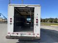 A 2012 Ford Econoline van with an open back revealing a spacious, empty interior and shelves along the sides