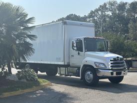 A 2012 Hino 338 truck with a white box body and chrome grille parked on a roadway