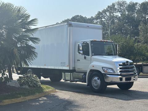 A 2012 Hino 338 truck with a white box body and chrome grille parked on a roadway