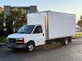 A white 2015 GMC Savana box truck with a large rectangular cargo area and a single cab is parked on a street