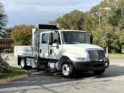 A white 2012 International 4300 truck with a flatbed and side mirrors parked on a road