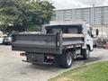 A white 2015 Mitsubishi Fuso FE160 truck with a flatbed and black dump body parked with its tailgate down