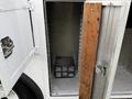 A 2005 Freightliner M2 106 with an open side compartment displaying a black storage unit inside