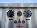Gauges on a metal panel displaying compound and pressure readings with indicators for low oil and high temperature along with an emergency engine stop button