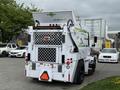 A white 2012 Global M4 street sweeper with a rear-facing broom and diamond-pattern grill, featuring green and black branding on its body
