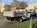 A 2006 Ford F-550 with a flatbed and side storage compartments parked with a dump bed raised