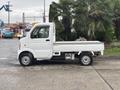 A white 2008 Suzuki Carry mini truck with a flatbed and a compact design is parked with flowers in the bed