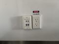 A wall outlet with three sockets including two USB ports labeled NET 12 and NET 11 and a warning sign indicating 115 volts