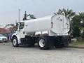 A white 2006 Freightliner M2 106 tanker truck with a rounded tank and a rear discharge pipe, featuring large black tires and two rear lights