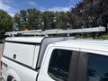 A 2019 Ford F-150 with a white truck bed cap and a metal ladder rack mounted on top positioned above the truck's cab