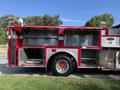A 1992 Emergency One Typhoon Superior fire truck with red and silver exterior featuring open compartments for equipment storage and a visible wheel on the side