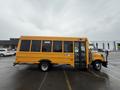 A yellow 2021 Ford Econoline bus with large windows and a side entrance door parked in a lot