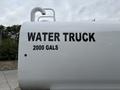 A white water truck with bold black lettering that reads "WATER TRUCK" and "2000 GALS" on its side