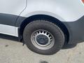 A close-up view of a 2025 Mercedes-Benz Sprinter's tire and wheel showcasing a silver rim with circular holes and a rugged black tire tread