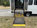A ramp from a 2014 Ford E-350 wheelchair accessible van positioned on grass with yellow safety markings and a metal surface