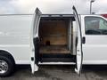 A 2022 GMC Savana van with its rear double doors open revealing a spacious empty cargo area with a wooden floor and shelving along the interior wall