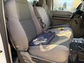 Interior view of a 2010 Ford F-550 showing the front bench seat upholstered in gray fabric with a black bag on the seat and a few items on the floor