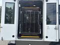 A 2020 Chevrolet Express van with an open rear door revealing a wheelchair lift featuring a metal mesh cage and a yellow platform ready for use