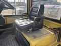 A black leather seat with a metal armrest on a yellow industrial vehicle interior