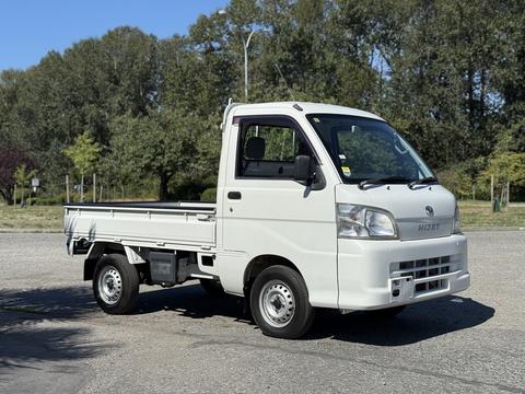 A white 2009 Daihatsu Hijet mini truck with a flatbed and a single cab parked on a gravel surface