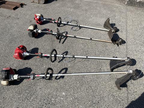 Three Shindaiwa gas-powered weed eaters displayed in a row with curved shafts and various cutting attachments