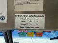 A sign inside a vehicle displaying dimensions and instructions with the text "CHECK YOUR SURROUNDINGS" and "Good Drivers Just Drive"