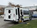 A white 2009 Ford Econoline bus with an open wheelchair ramp and two rear doors ajar