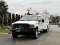 A 2001 Ford F-350 with a white body and a utility bed featuring a raised aerial platform and orange lights on the roof