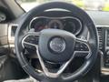 A close-up of the steering wheel of a 2015 Jeep Grand Cherokee featuring the Jeep logo and various control buttons on the wheel
