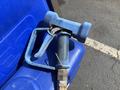 A blue fuel nozzle with a textured grip and a metal clip resting on a blue surface