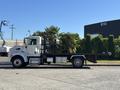A 2020 Peterbilt 330 truck with a black flatbed and chrome accents parked on a street with greenery nearby