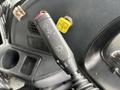 A close-up of a black gear stick lever featuring directional arrows for left and right signaling along with a light switch marked with a sun symbol.