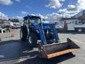 A blue 2010 New Holland T4050 tractor with a front loader attachment parked in a lot with other vehicles visible in the background