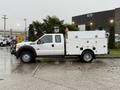 A white 2015 Ford F-450 truck with a utility bed and mounted yellow light on top parked in a wet area