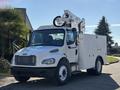 A white 2005 Freightliner M2 106 utility truck with a raised aerial work platform and multiple compartments on the side