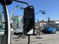 A 2016 Isuzu NPR-HD truck is parked with its side mirror prominently displayed reflecting part of the scene behind it