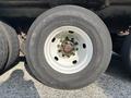 A close-up of a large black tire mounted on a white rim showing rusted bolts and green corrosion on the wheel hub