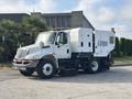 A 2012 International DuraStar 4300 street sweeper truck with a white body and black wheels equipped with brushes and a debris container