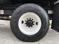A close-up of the wheel of a 2021 Freightliner M2 106 featuring a black tire with white rim and several bolt holes in the center