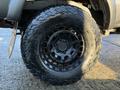 A close-up view of a black alloy wheel on a 2004 Toyota Tacoma featuring a rugged tire with deep treads designed for off-road driving