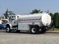 2010 Freightliner M2 106 tanker truck with a silver tank and red stripes on the side parked on a concrete surface