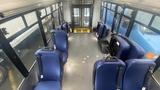 Interior view of a 2021 Ford Transit with blue upholstered seats arranged in rows facing forward and an empty aisle leading to the rear door