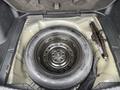 A spare tire mounted on a black rim with a jack located beside it inside the storage compartment of a 2014 Honda CR-V