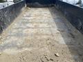 A 2014 PJ 16 Foot Dump Trailer with a sandy and rocky surface inside the cargo area